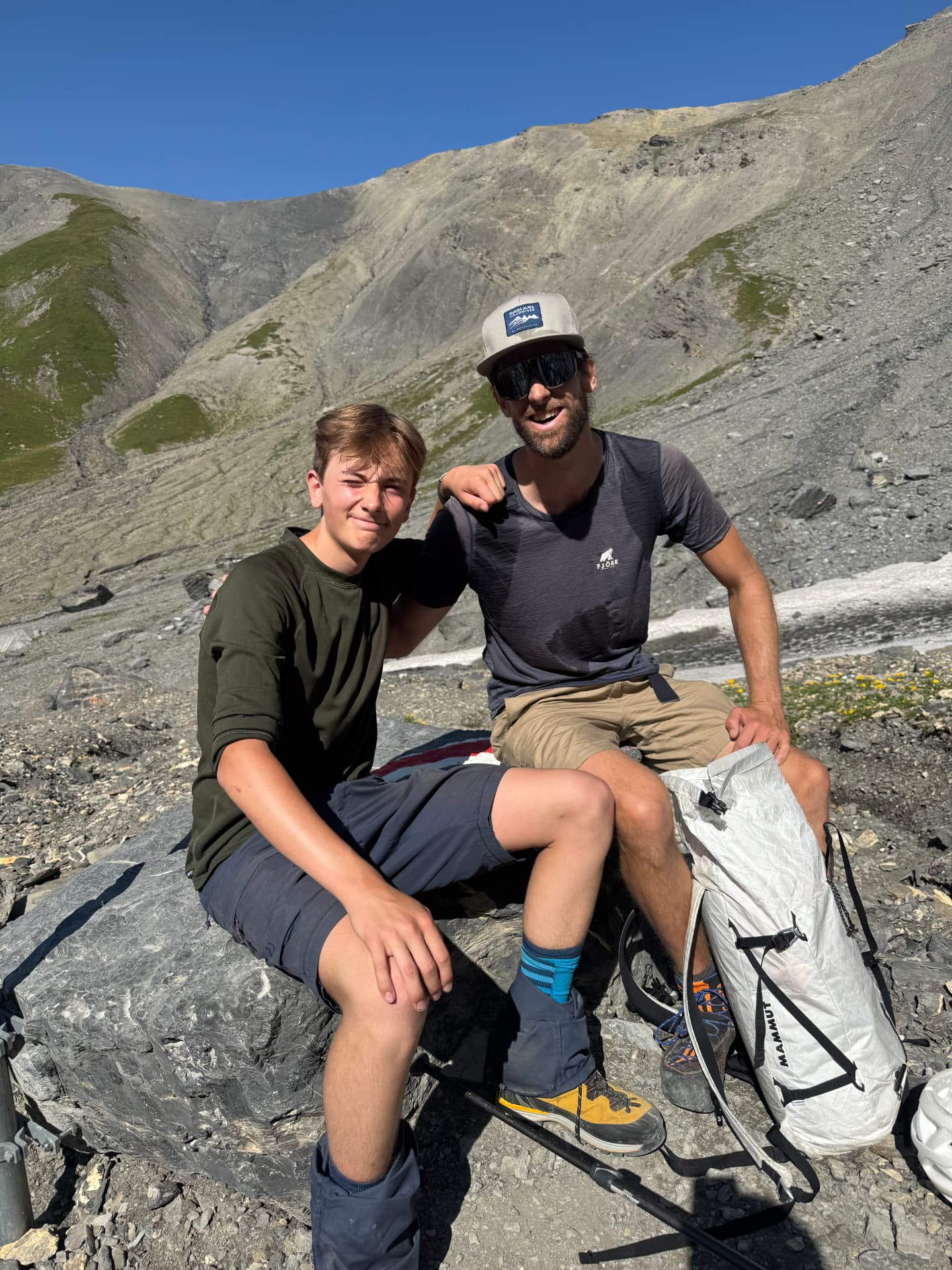 Quentin, guide de montagne, assis sur un rocher avec un jeune client lors d'une course en montagne