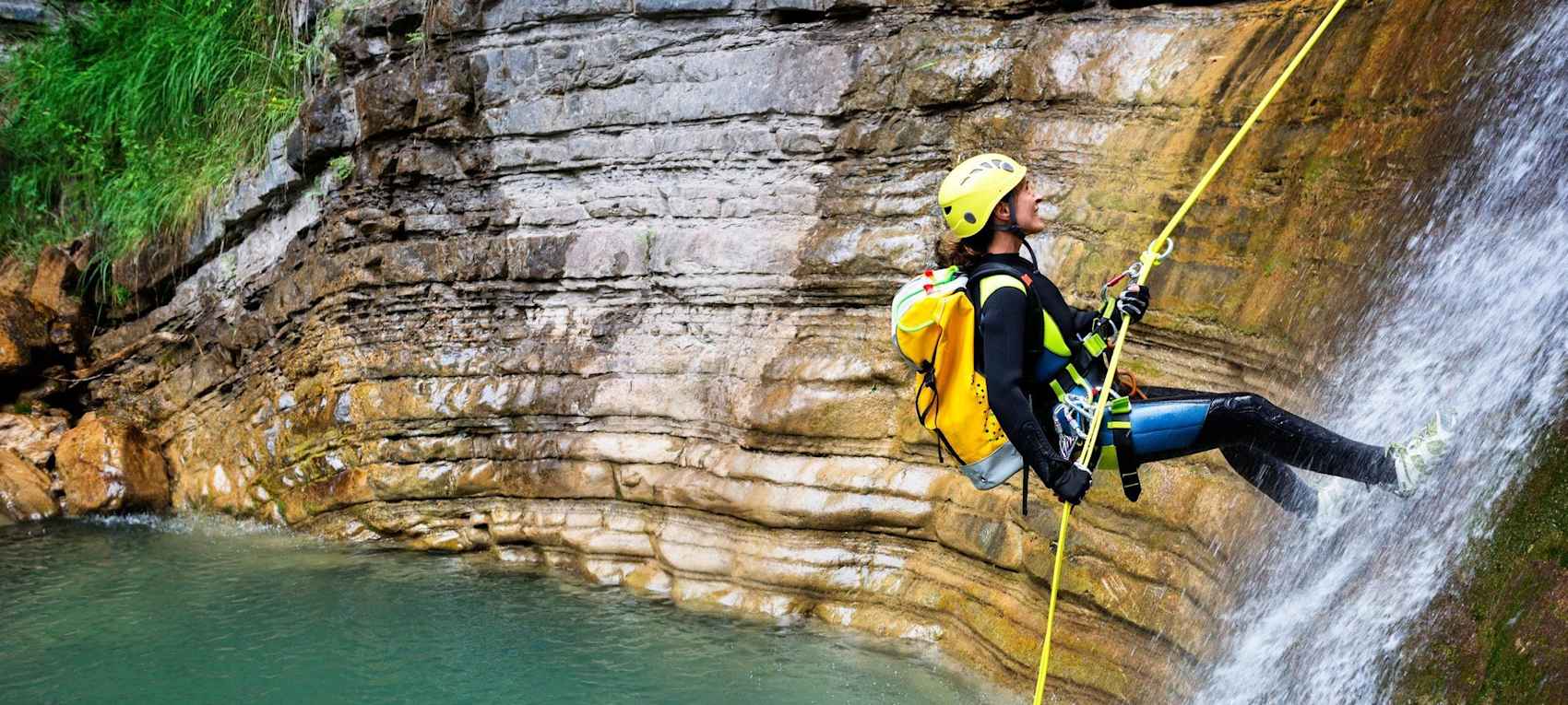 Canyoniste en combinaison descendant en rappel dans une cascade au-dessus d'une vasque turquoise